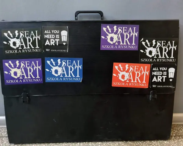 Czarna walizka na prace plastyczne ozdobiona naklejkami "SEAL ART SZKOŁA RYSUNKU" i "ALL YOU NEED IS ART".