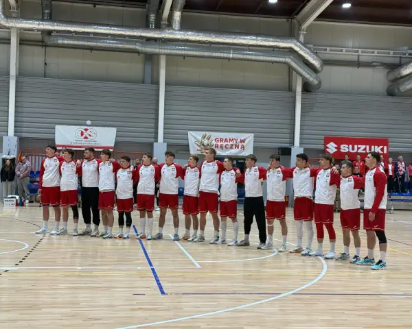 Drużyna w strojach biało-czerwonych, w tym Filip Jankowski, stoi na parkiecie hali sportowej.