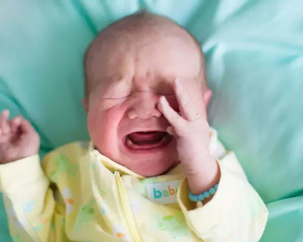 Ein **baby weinen** auf einem türkisfarbenen Tuch, mit geschlossenen Augen und einer Hand vor dem Gesicht.