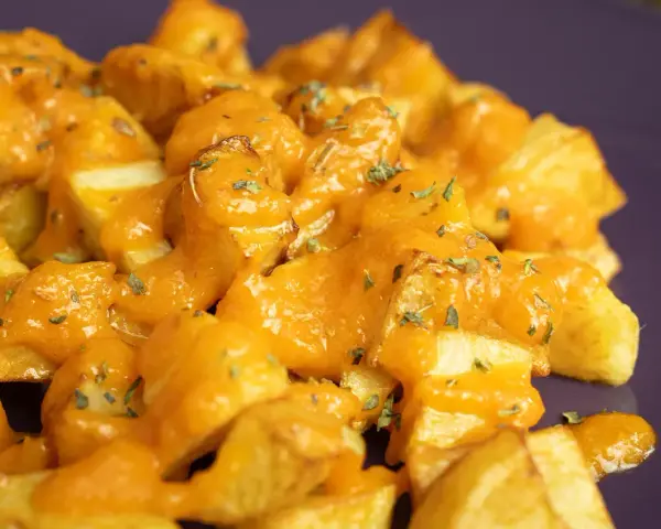 Patatas bravas crujientes cubiertas con una salsa naranja cremosa y hierbas picadas.