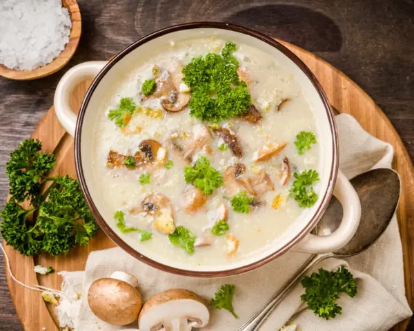 Kremowa zupa pieczarkowa, przepis babci, z kawałkami pieczarek i natką pietruszki. Obok miseczka z solą i świeże pieczarki.