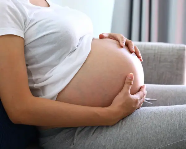 Kobieta w ciąży trzyma dłonie na brzuchu, zastanawiając się, jak przyspieszyć poród.