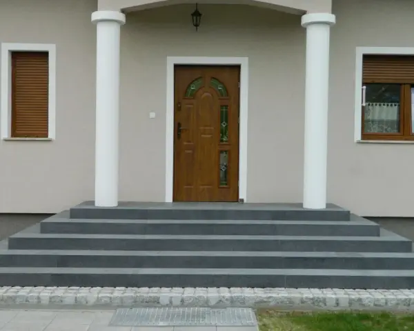 Elegancka, zewnętrzna klatka schodowa w domu jednorodzinnym prowadzi do brązowych drzwi z witrażem.