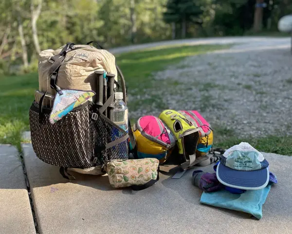Ready for adventure! This ultralight backpacking gear list includes a tan pack, colorful stuff sacks, trekking poles, a water bottle, and a hat.