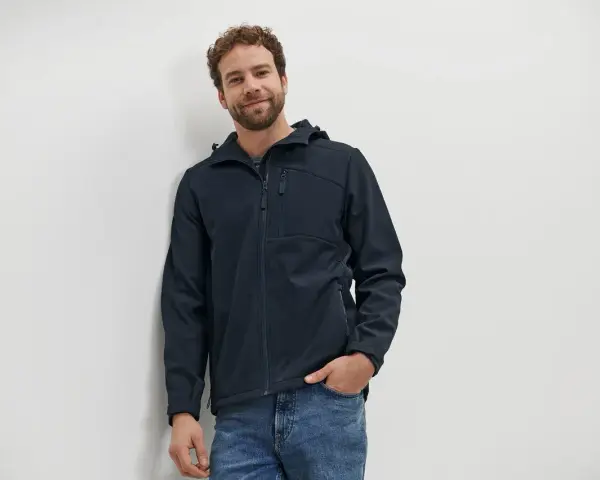 Mann mit lockigem Haar trägt eine dunkelblaue Softshelljacke und Jeans. Perfekt für das nächste Abenteuer oder zum Softshelljacke waschen.