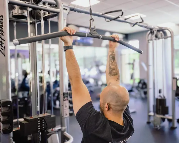 Man med tatueringar utför enarms latsdrag på ett gym.