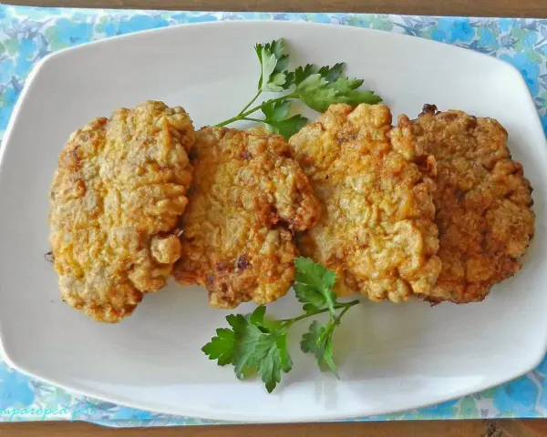 Cuatro filetes rusos dorados y crujientes servidos en un plato blanco con perejil.