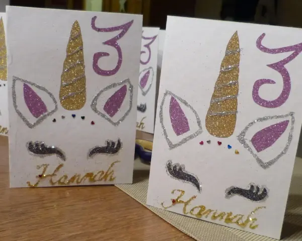 Glitzernde Einhorn-Einladungen zum 3. Geburtstag basteln. Hannahs Name ist in Goldbuchstaben geschrieben.
