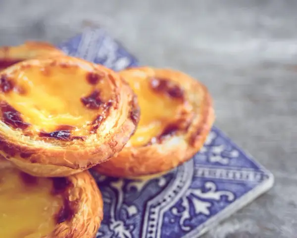 Ein Stapel goldbrauner, karamellisierter Pastel de Nata auf einer blauen Kachel.