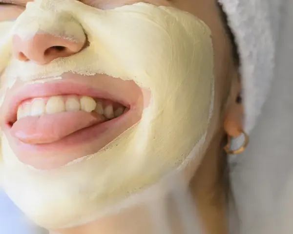 Una mujer se divierte con una mascarilla facial amarilla, sacando la lengua.
