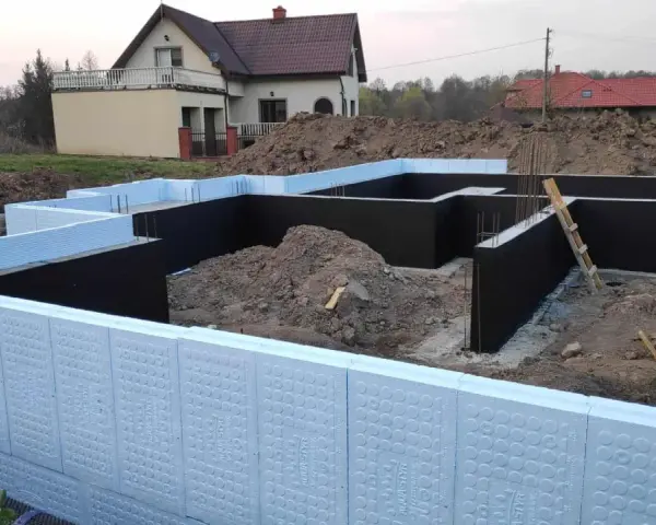 Budowa domu: jak ocieplić fundament styropianem. Widoczne elementy izolacji fundamentów, zbrojenia i ziemia.