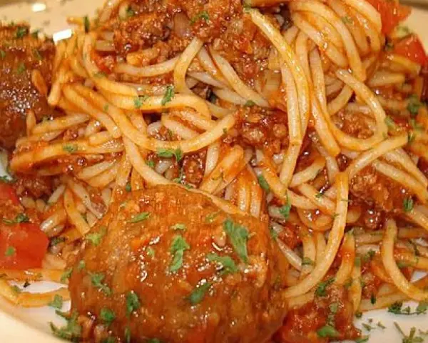 Pyszne spaghetti z pulpetami w sosie pomidorowym, posypane natką pietruszki. Klasyczne danie, które zawsze smakuje wyśmienicie.