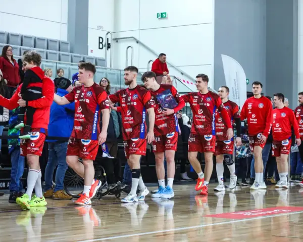 Drużyna kwidzyn piłka ręczna w czerwonych strojach wchodzi na halę, pozdrawiając kibiców.