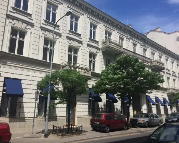 Kamienica z balkonami i niebieskimi markizami. Zastanawiasz się, dlaczego koszt czynszu w blokach z 2026 roku jest wyższy niż w kamienicach?