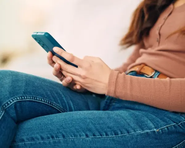 Kobieta w dżinsach i bluzce z długim rękawem trzyma telefon. To może być obraz skutków zbyt długiego korzystania z telefonu.