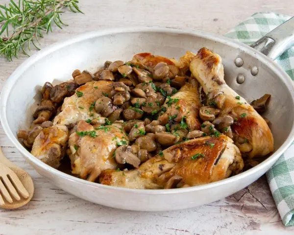 Delizioso pollo con funghi in padella, guarnito con prezzemolo fresco e accompagnato da rosmarino.