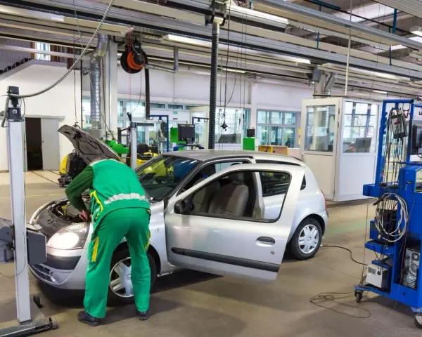 Un meccanico in tuta verde controlla un'auto argentata in un'officina, forse per un controllo secondo l'articolo 80 del codice della strada.