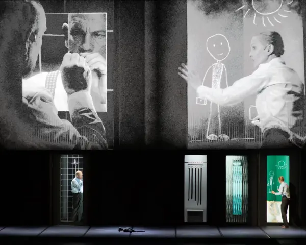 Scena teatralna z projekcjami. Na górze czarno-białe obrazy mężczyzn i kobiety rysującej słońce. Na dole, w oknach, samotność pól bawełnianych, mężczyzna w klatce, przedmioty i kobieta rysująca.