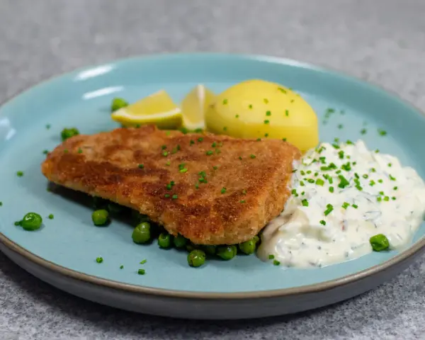 Panerad fisk med kokt potatis, ärtor och en krämig kall sås till fisk, garnerad med gräslök och citronklyftor.