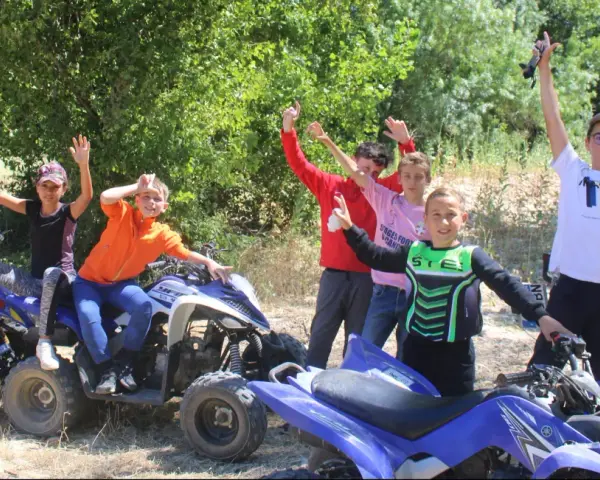 Des enfants joyeux sur des quads, bras levés, en extérieur.