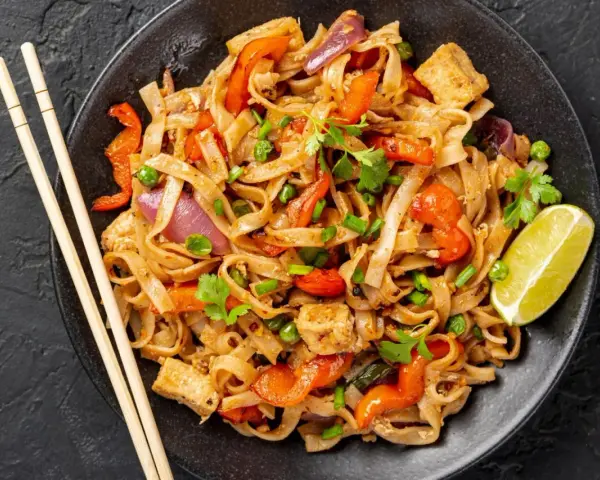 Pyszne pad thai kai z kurczakiem, makaronem ryżowym, warzywami i limonką. Idealne danie na szybki obiad.