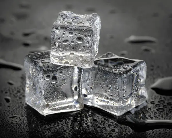 Drei eiswürfel mit Wassertropfen auf schwarzem Hintergrund. Die Frage, wie lange braucht Eis zum Gefrieren, wird hier visuell beantwortet.