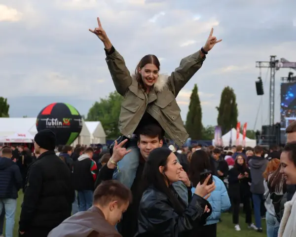 Dziewczyna na ramionach chłopaka cieszy się na Juwenaliach Politechniki Lubelskiej. W tle scena i tłum bawiących się studentów.