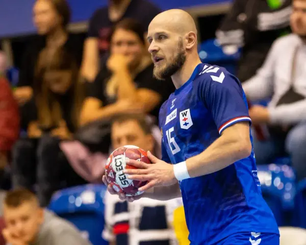 Mateusz Jachlewski, szczypiornista w niebieskiej koszulce z numerem 15, trzyma piłkę do piłki ręcznej.