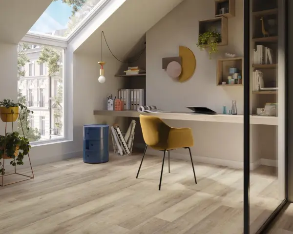 Luminoso studio mansardato con scrivania, sedia gialla e un elegante **pavimento polvere di pietra** che riflette la luce naturale.