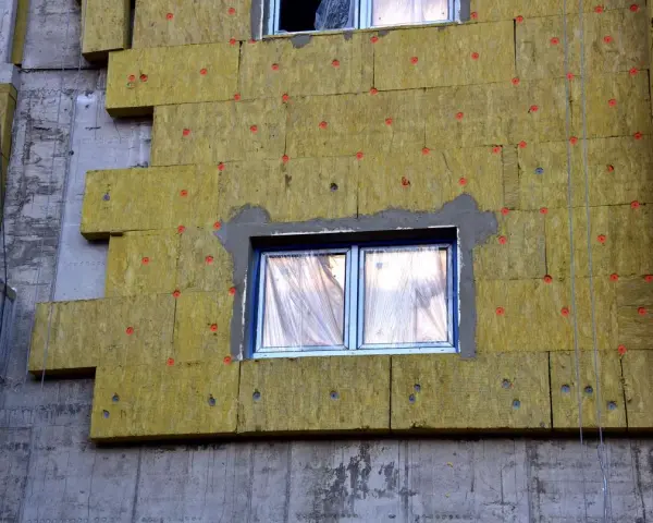 Pannelli di lana di roccia per cappotto termico spessore, fissati con tasselli rossi su un edificio in costruzione.