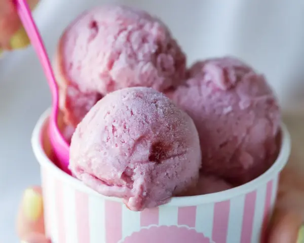 Różowe lody w kubeczku, z różową łyżeczką. Zastanawiasz się, ile kalorii mają lody?