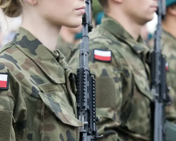 Żołnierze w mundurach z polskimi flagami, gotowi do marszu. Słychać przyśpiewki wojskowe.