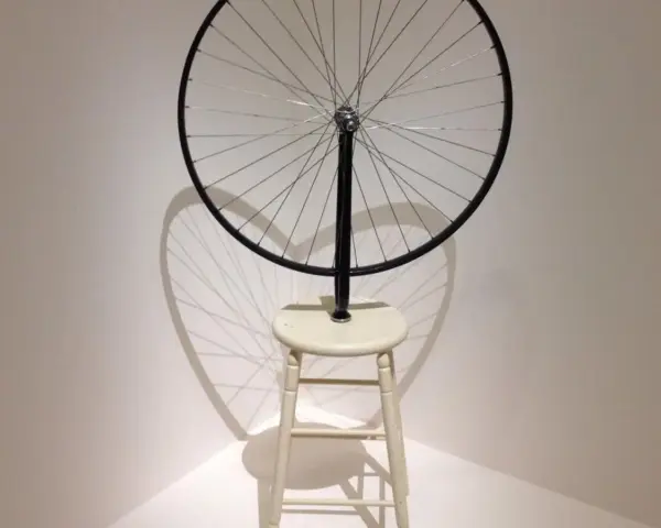 Roue de vélo fixée sur un tabouret, une œuvre emblématique de Marcel Duchamp, projetant une ombre fascinante.