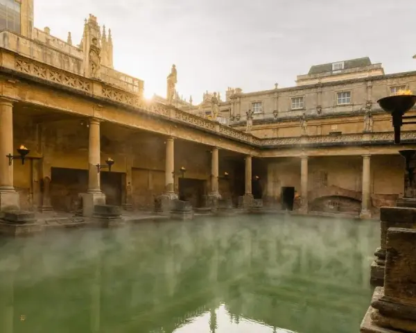 Steaming green water fills the Great Bath, surrounded by ancient Roman ruins with columns and torches.
