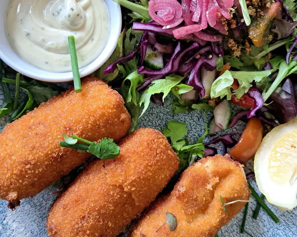 Croquetas doradas y crujientes con ensalada fresca, salsa y limón.