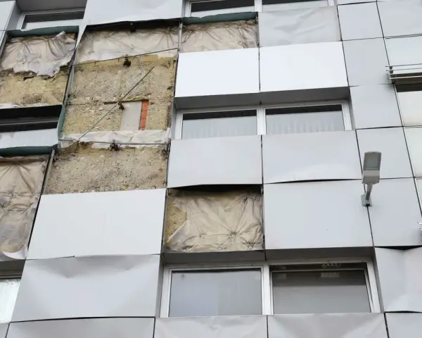 Facciata di un edificio con pannelli rimossi, mostrando l'isolamento. Si valuta la conducibilità termica dei materiali per l'efficienza energetica.