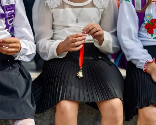 Trzy dziewczynki w szkolnych strojach, jedna trzyma dzwoneczek na wstążce. Czy w klasie 1-3 są świadectwa z paskiem?