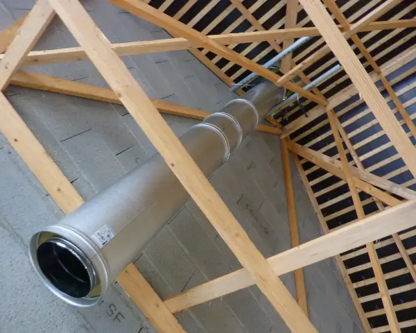 Installation d'un tubage cheminée en métal dans une charpente en bois. Le conduit traverse un mur en parpaings.