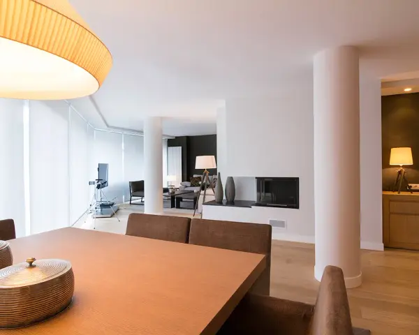 Comedor y salón modernos tras reforma piso pequeño. Mesa de madera, chimenea y mobiliario elegante.