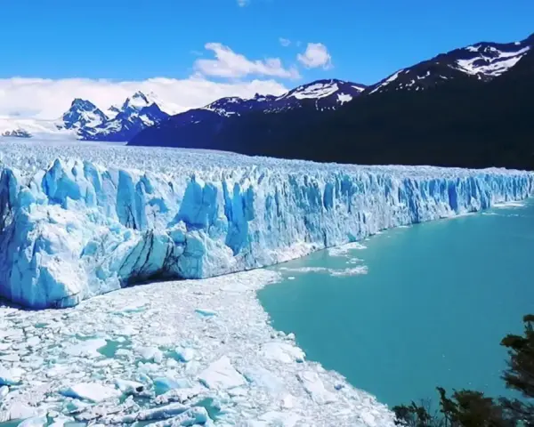 Impresionante glaciar Perito Moreno, con sus paredes de hielo azul intenso y el agua turquesa del lago. Montañas nevadas al fondo.
