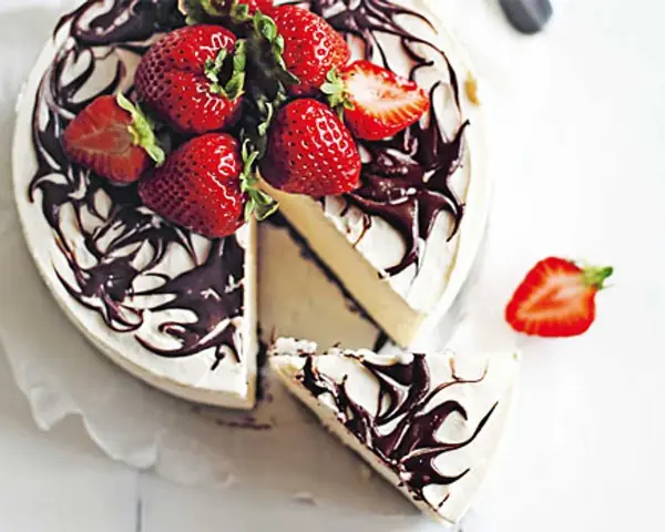 En krämig no bake cheesecake med chokladdrizzle och färska jordgubbar. En bit är uppskuren.