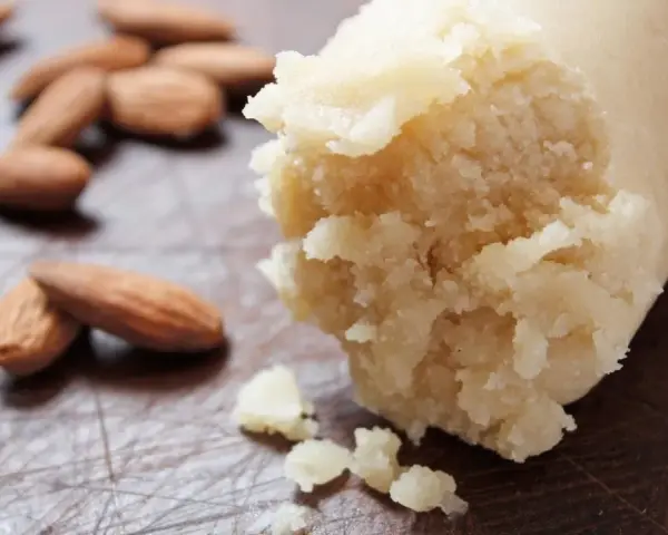 Frische Mandeln liegen neben einer Rolle Marzipan Rohmasse, bereit zum Verarbeiten.