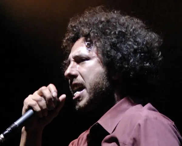 Zack de la Rocha heute, mit seinem charakteristischen lockigen Haar und einem Mikrofon in der Hand, singt leidenschaftlich auf der Bühne.