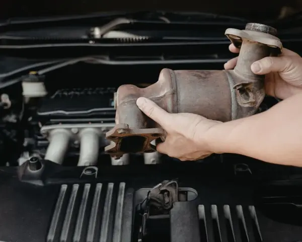 Mani che rimuovono un catalizzatore arrugginito dal vano motore di un'auto. Riparazione del fap auto.