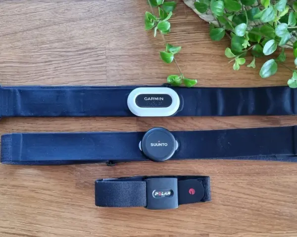 Tre pulsbands från Garmin, Suunto och Polar ligger på ett trägolv. Jämför garmin pulsband skillnad med de andra.