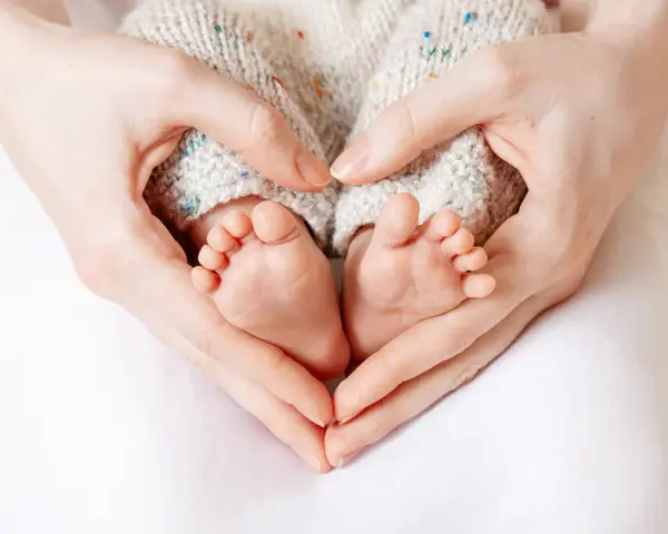 Manos formando un corazón alrededor de los pies de un bebé, evocando la protección y el complemento de maternidad con retroactividad.