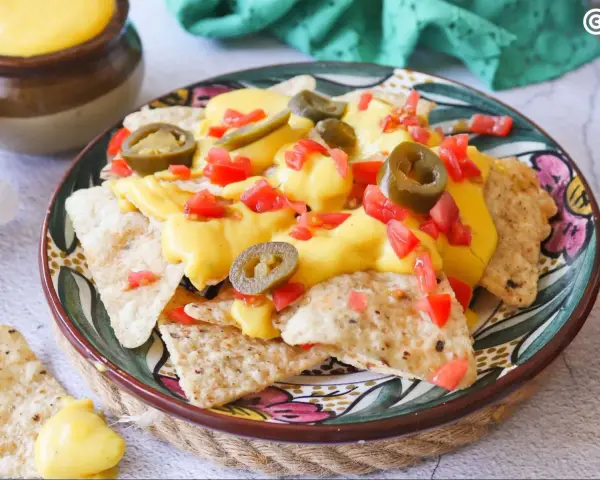 Nachos con queso derretido, jalapeños y tomate picado en un plato decorado.