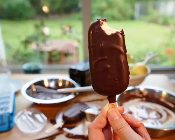 Ein abgebissener Schokoriegel, der zeigt, wie einfach es ist, Magnum Eis selber machen. Zutaten und Eisformen liegen bereit.
