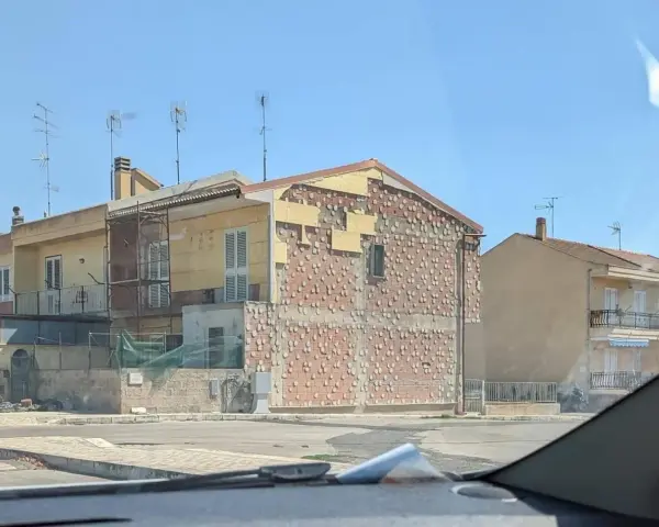 Edificio in fase di ristrutturazione, con facciata parzialmente scoperta che rivela la muratura. Sembra un condominio in attesa del suo nuovo cappotto.