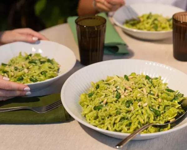 Due piatti di trofie al pesto, condite con fagiolini e pinoli, pronte per essere gustate.